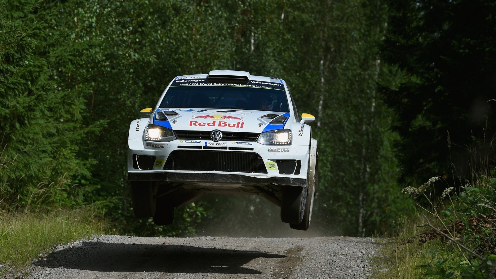 Ralliauto hyppää soratiellä yleisön edessä Jyväskylän MM-rallin erikoiskokeella.